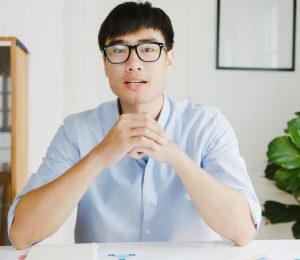Young Asia businessman using computer laptop talk to colleagues Young Asia businessman using computer laptop talk to colleagues about plan in video call meeting while working from home at living room. Self-isolation, social distancing, quarantine for corona virus.